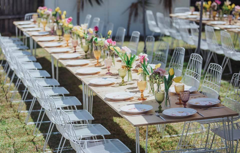 backyard table set up with white wire chairs, floral decorations and white hairpin banquet tables