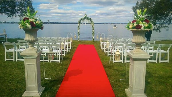 red carpet at a wedding ceremony venue with white padded folding chairs and floral bridal arch