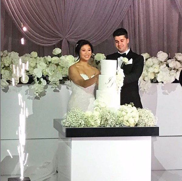 husband and wife cutting cake that is placed on top of gloss cake table