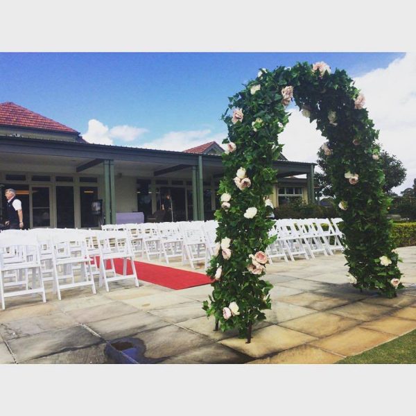 red carpet at an outdoor wedding ceremony. White padded folding chairs and a floral bridal arch