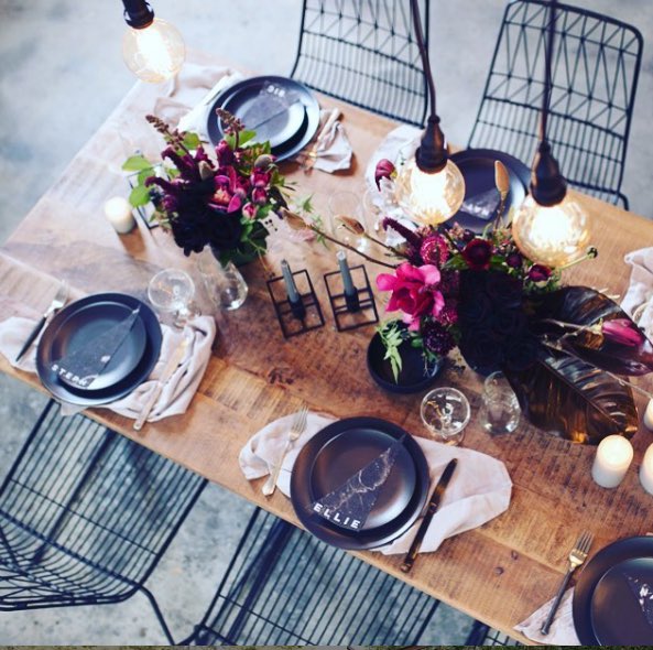 timber table decorated with cutlery and plates. black wire chairs and flowers